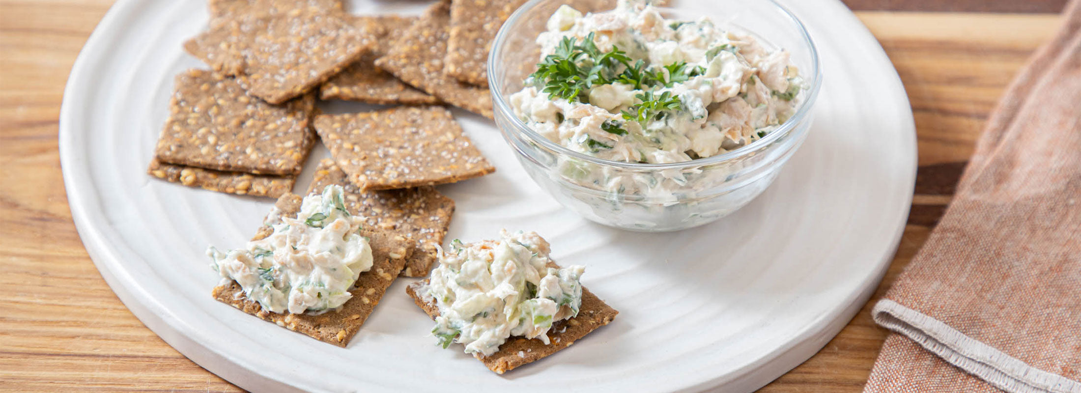 A small bowl of Wild Salmon Spread made with Patagonia Provisions' Wild Pink Salmon rests on a white plate next to Breadfruit crackers topped with dip